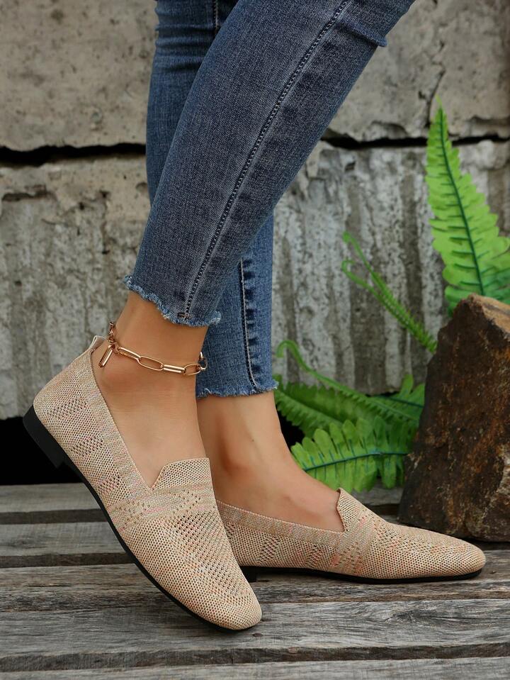 Profil d'une paire beige en maille tricotée portée avec un jean effrangé, devant un mur de pierre et une fougère. 4