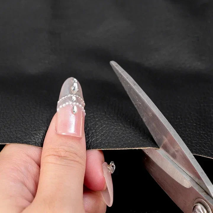 Ciseaux découpant un bord du cuir noir à la taille voulue, main aux ongles ornés 5