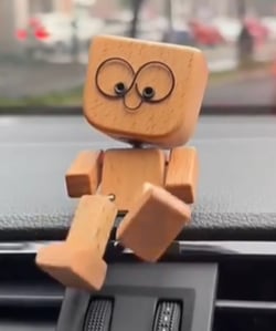 Gros plan sur le personnage en bois aux yeux ronds, assis sur un tableau de bord de voiture, jambes pendantes. 6