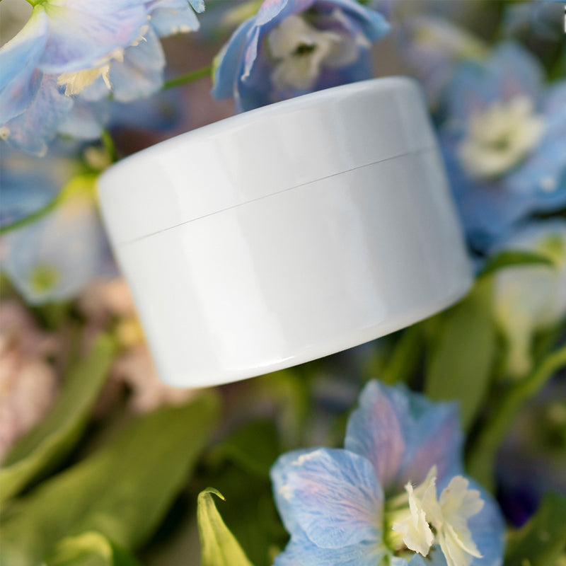 Insert blanc à couvercle posé sur des fleurs bleues de delphinium et du feuillage vert. 15