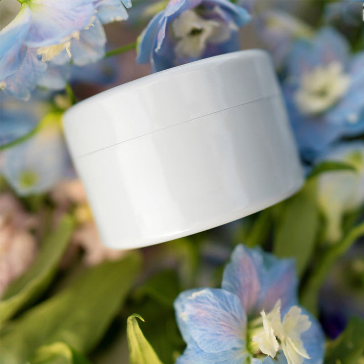Insert blanc à couvercle posé sur des fleurs bleues de delphinium et du feuillage vert. 15