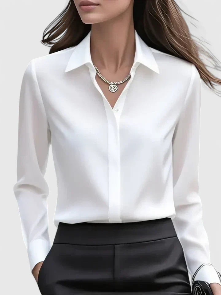 Vue de face du chemisier blanc à col chemise, porté avec un pantalon noir et un collier argenté. 2