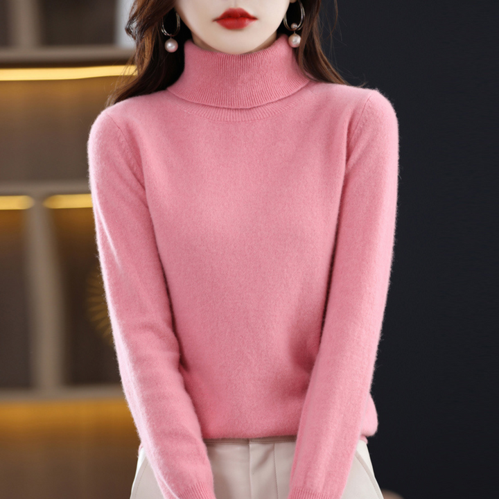 Pull rose à col roulé porté par une femme, bras le long du corps, associé à un pantalon clair. 7