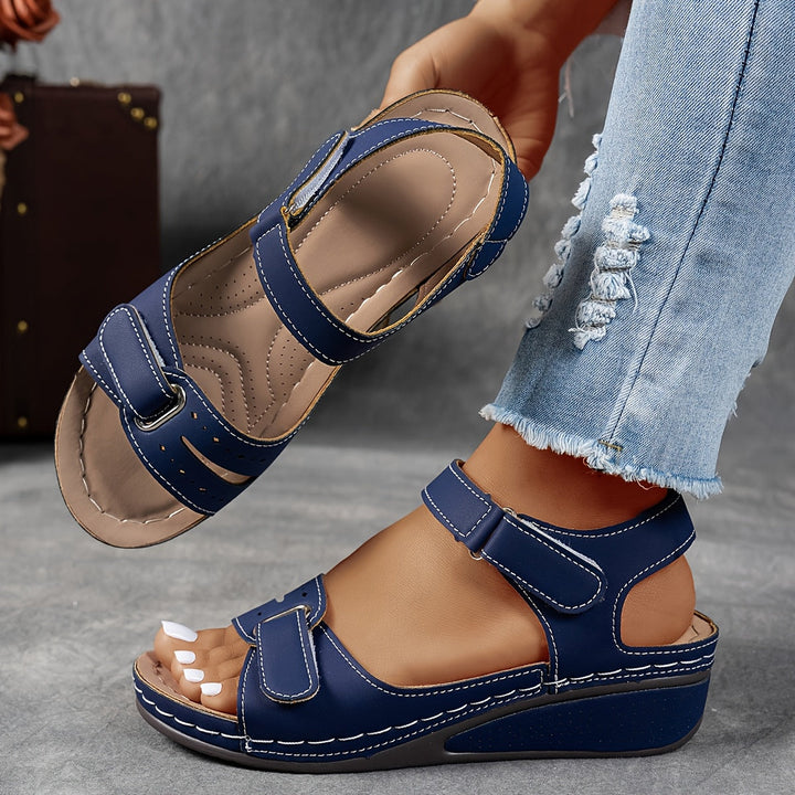 Sandales compensées bleu marine à brides auto-agrippantes et surpiqûres claires, portées avec un jean déchiré, l'autre sandale présentant sa semelle matelassée. 8
