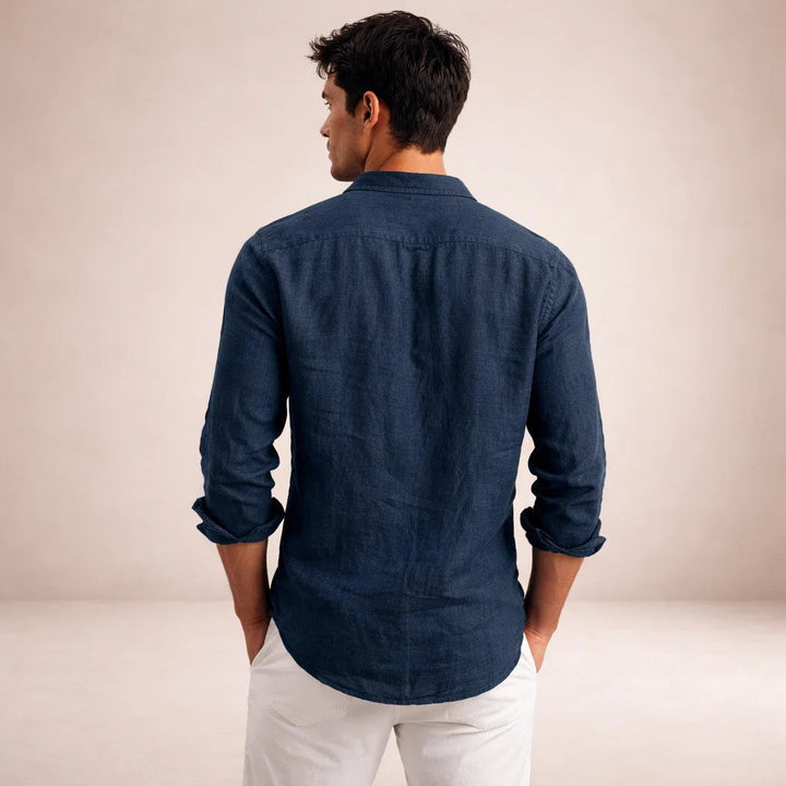 Vue de dos de la chemise en lin bleu marine portée par un homme, mains dans les poches du pantalon blanc. 13