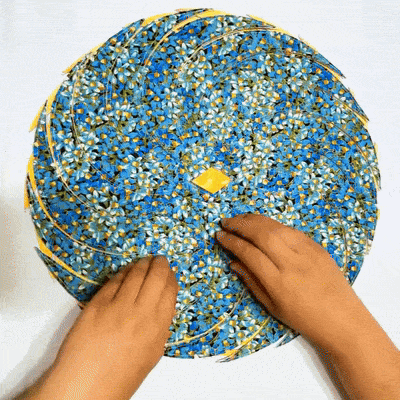 Deux mains assemblent sur une surface blanche les pièces d'un set de table circulaire en tissu fleuri bleu, étape de montage. 1