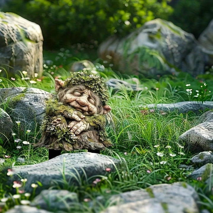 Tuteur du troll endormi aux mains croisées et couronne de feuilles, posé dans l'herbe parmi de gros rochers et de petites fleurs. 16