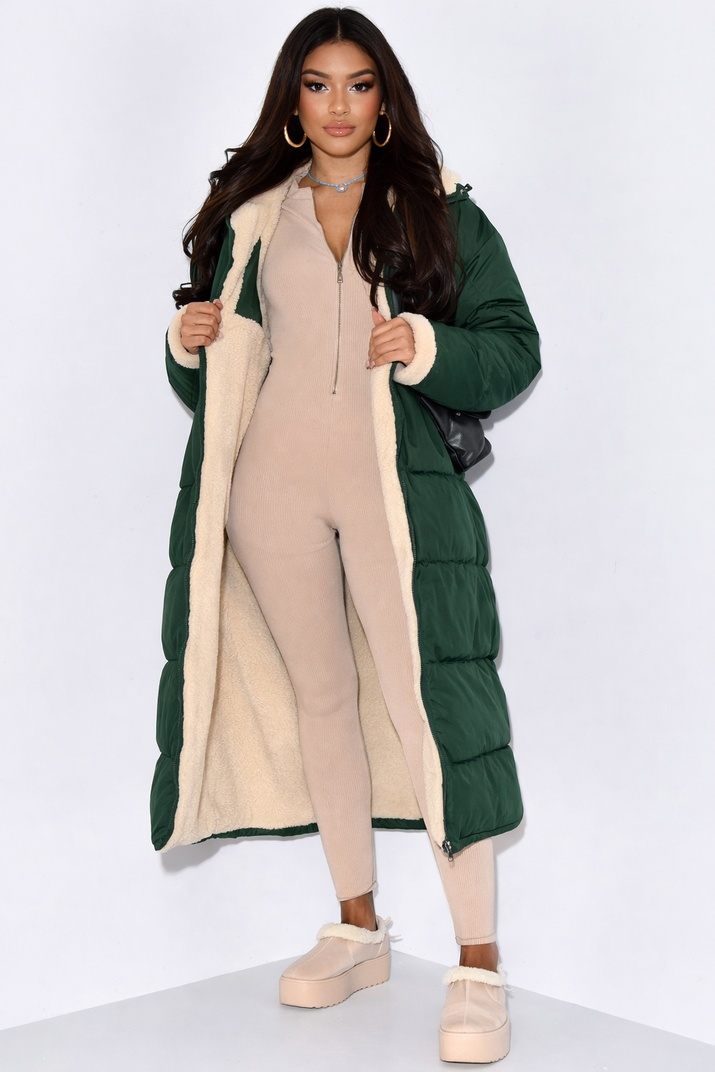 Femme portant le manteau matelassé vert foncé ouvert sur sa doublure en fourrure beige, avec une combinaison côtelée beige zippée. 3