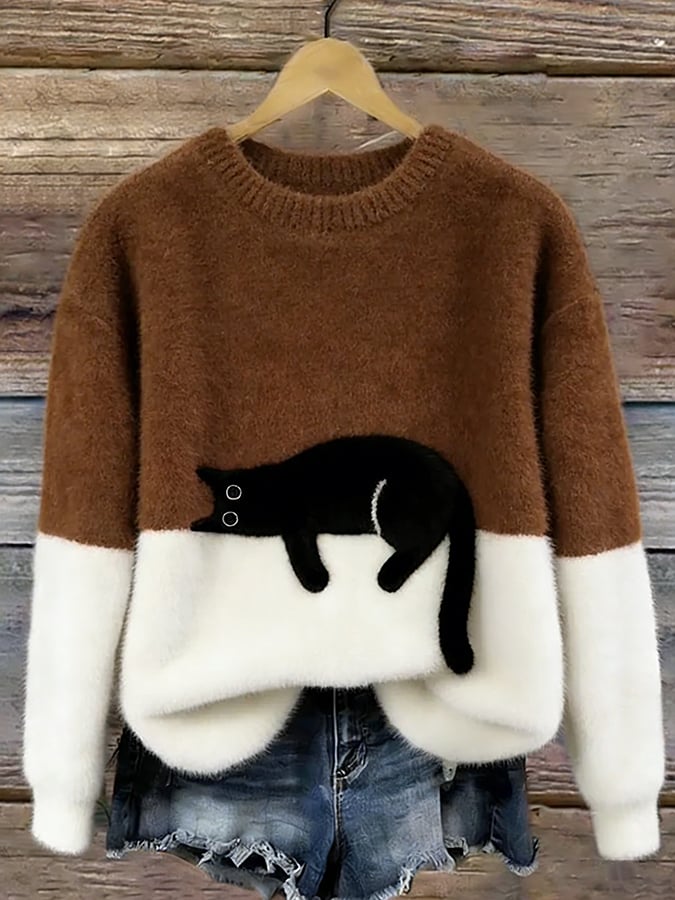 Version marron caramel et blanche du pull au chat noir étendu, suspendue sur un cintre devant un mur en bois. 10
