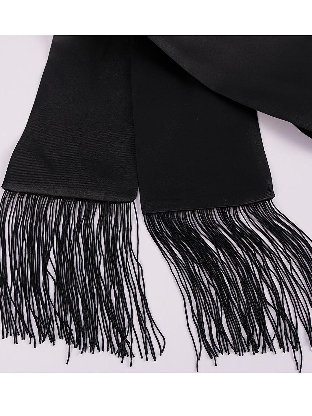 Gros plan sur les deux extrémités de la ceinture noire, terminées par de longues franges 8