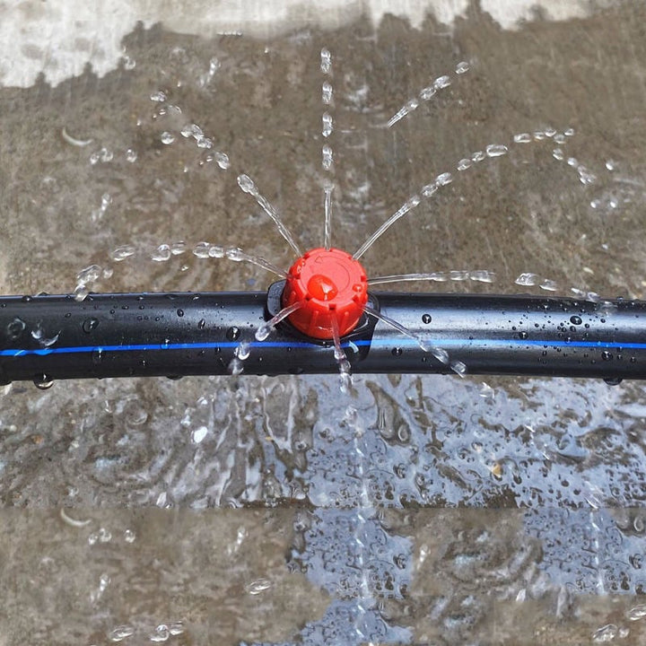 Goutteur rouge monté sur un tuyau noir à bande bleue, projetant l'eau en jets fins dans toutes les directions. 1