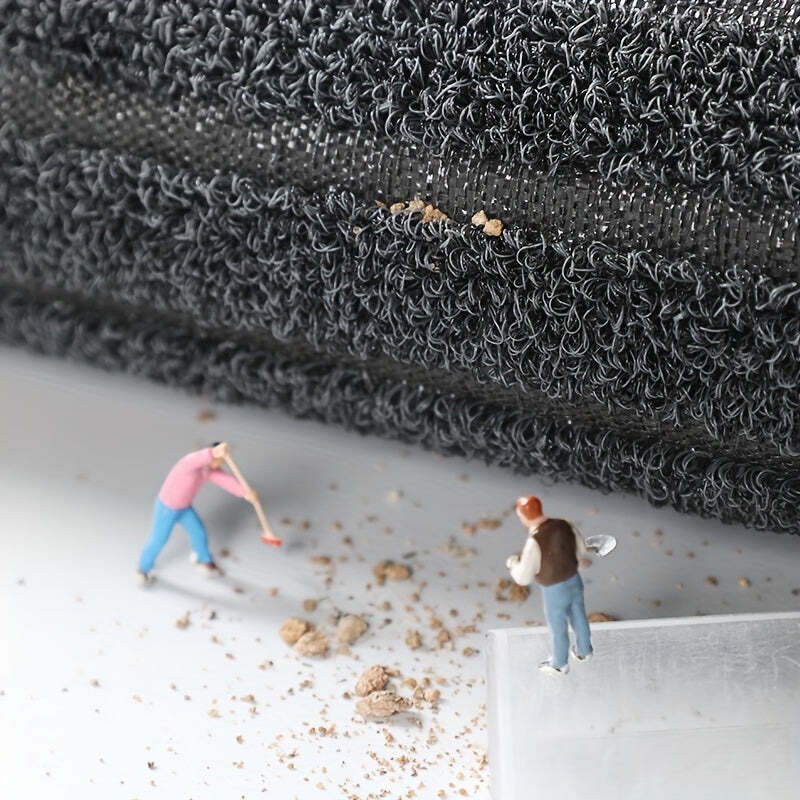 Bord du tapis soulevé laissant voir la sous-couche tissée, avec des figurines qui ramassent la terre tombée sur le sol. 6
