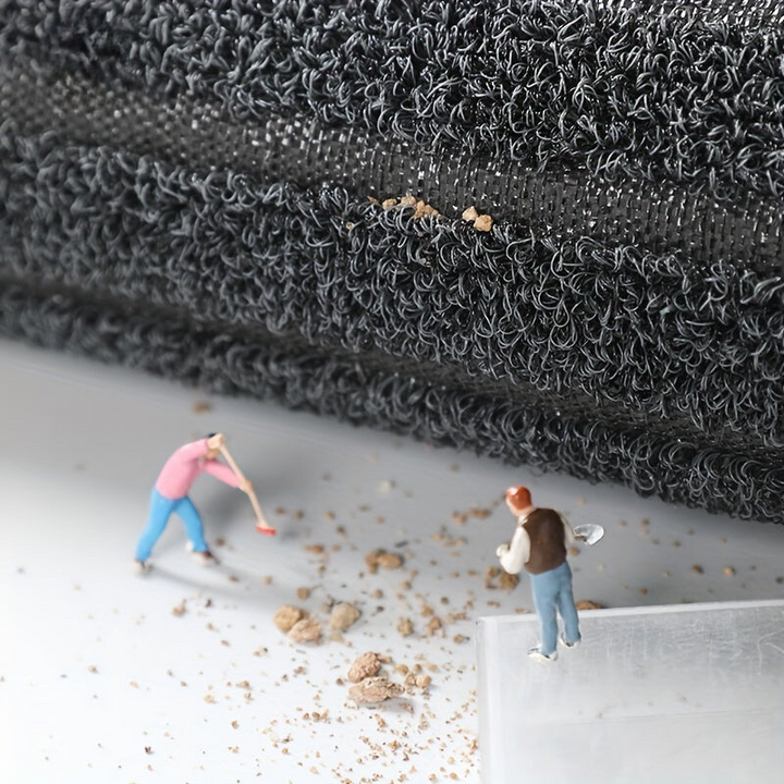 Bord du tapis soulevé laissant voir la sous-couche tissée, avec des figurines qui ramassent la terre tombée sur le sol. 6