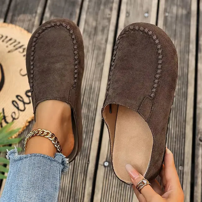 Mules marron foncé façon daim vues de dessus, une paire portée et l'autre tenue à la main pour montrer l'intérieur clair. 3