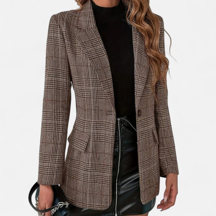 Vue de face rapprochée du blazer à carreaux marron porté ouvert avec un haut noir, une jupe en similicuir et un sac à main. 1