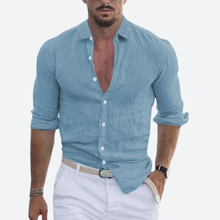 Chemise bleu grisé portée par un homme, col ouvert, manches retroussées, pantalon blanc et ceinture tressée. 1