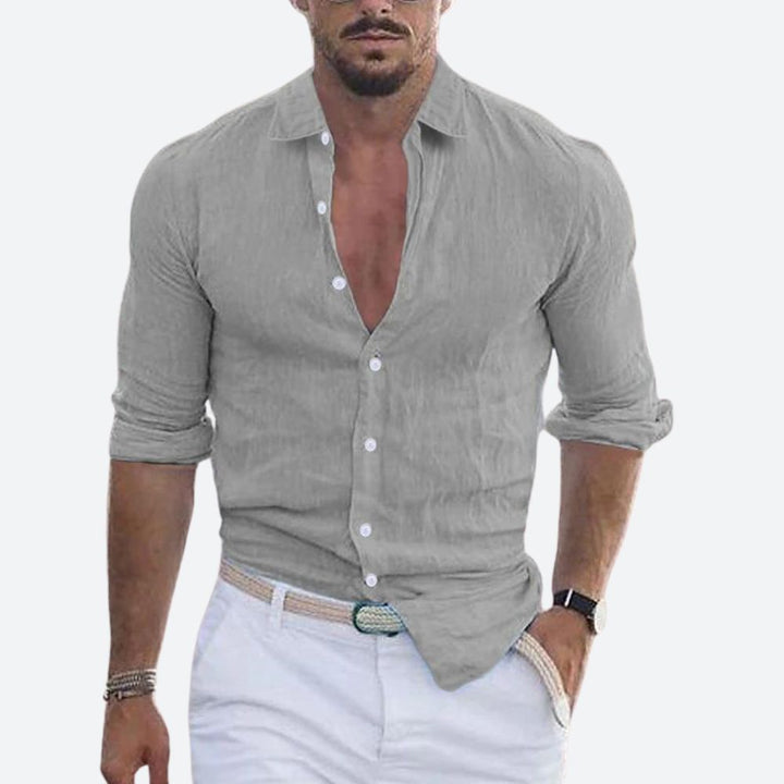 Chemise grise portée par un homme, col ouvert, manches retroussées, avec pantalon blanc et ceinture tressée. 6
