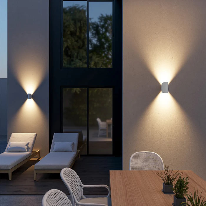 Appliques blanches éclairant vers le haut et le bas sur le mur d'une terrasse au crépuscule, avec transats et chaises tressées. 6