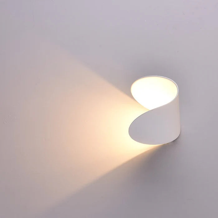 Applique blanche pivotée émettant un large faisceau de lumière chaude sur un mur clair, ouverture visible sur le dessus. 16