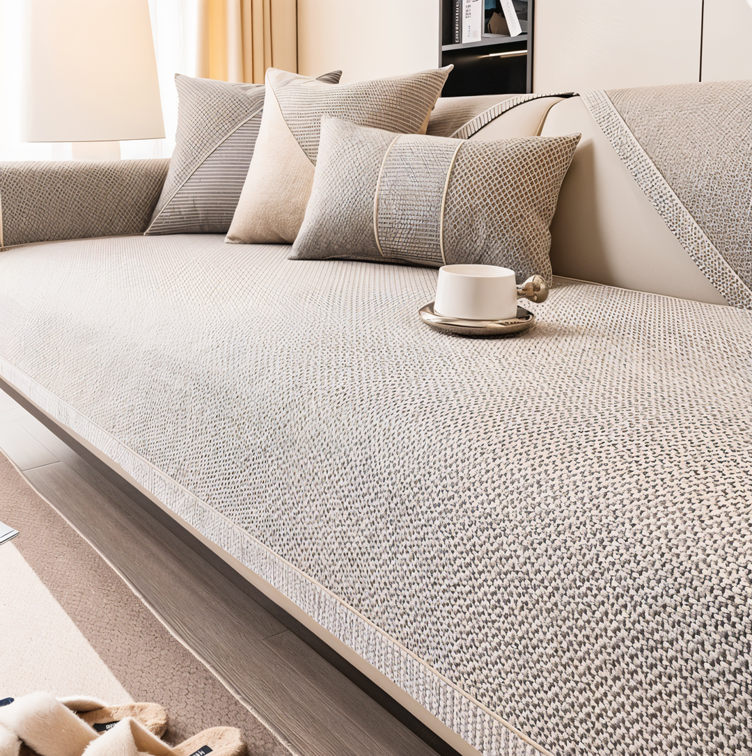Housse beige-gris en tissu texturé tendue sur l'assise d'un canapé, avec coussins assortis et une tasse blanche posée dessus. 1