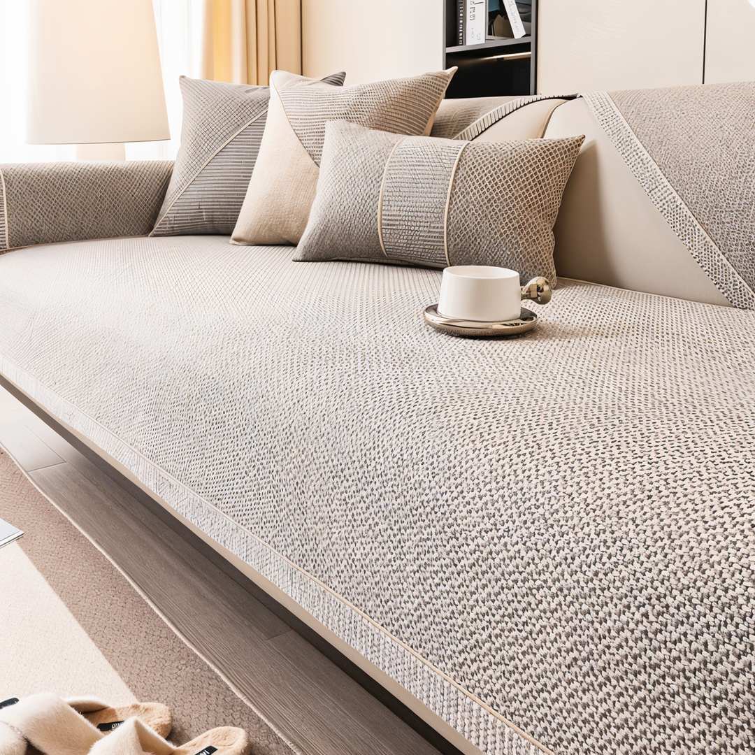 Vue large de la housse beige-gris sur le canapé, avec coussins coordonnés, accoudoir couvert et tasse blanche sur l'assise. 5