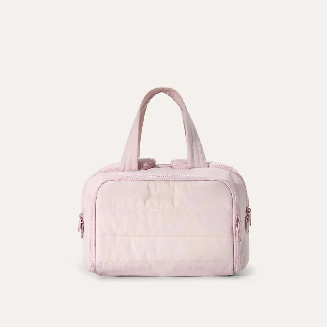 Vue de face de la trousse matelassée rose pâle avec deux anses souples et fermetures éclair sur les côtés. 1