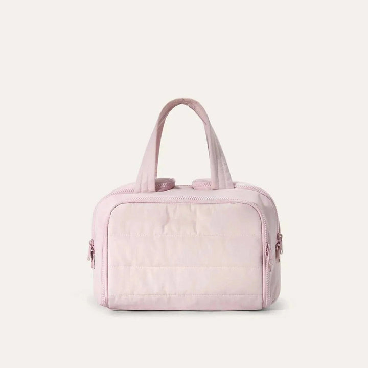 Vue de face de la trousse matelassée rose pâle avec deux anses souples et fermetures éclair sur les côtés. 1