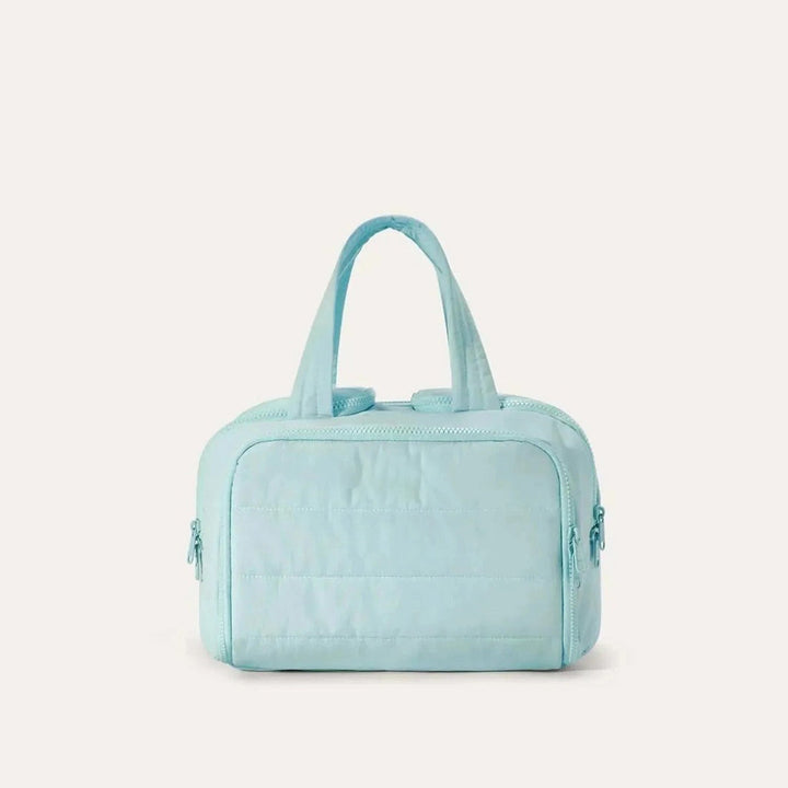 Trousse matelassée de face dans un coloris bleu turquoise clair, avec anses souples et fermetures éclair assorties. 15