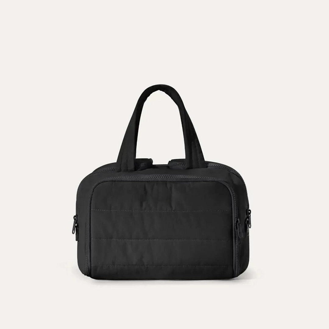 Trousse matelassée de face dans un coloris noir, avec anses souples et fermetures éclair sur les côtés. 14