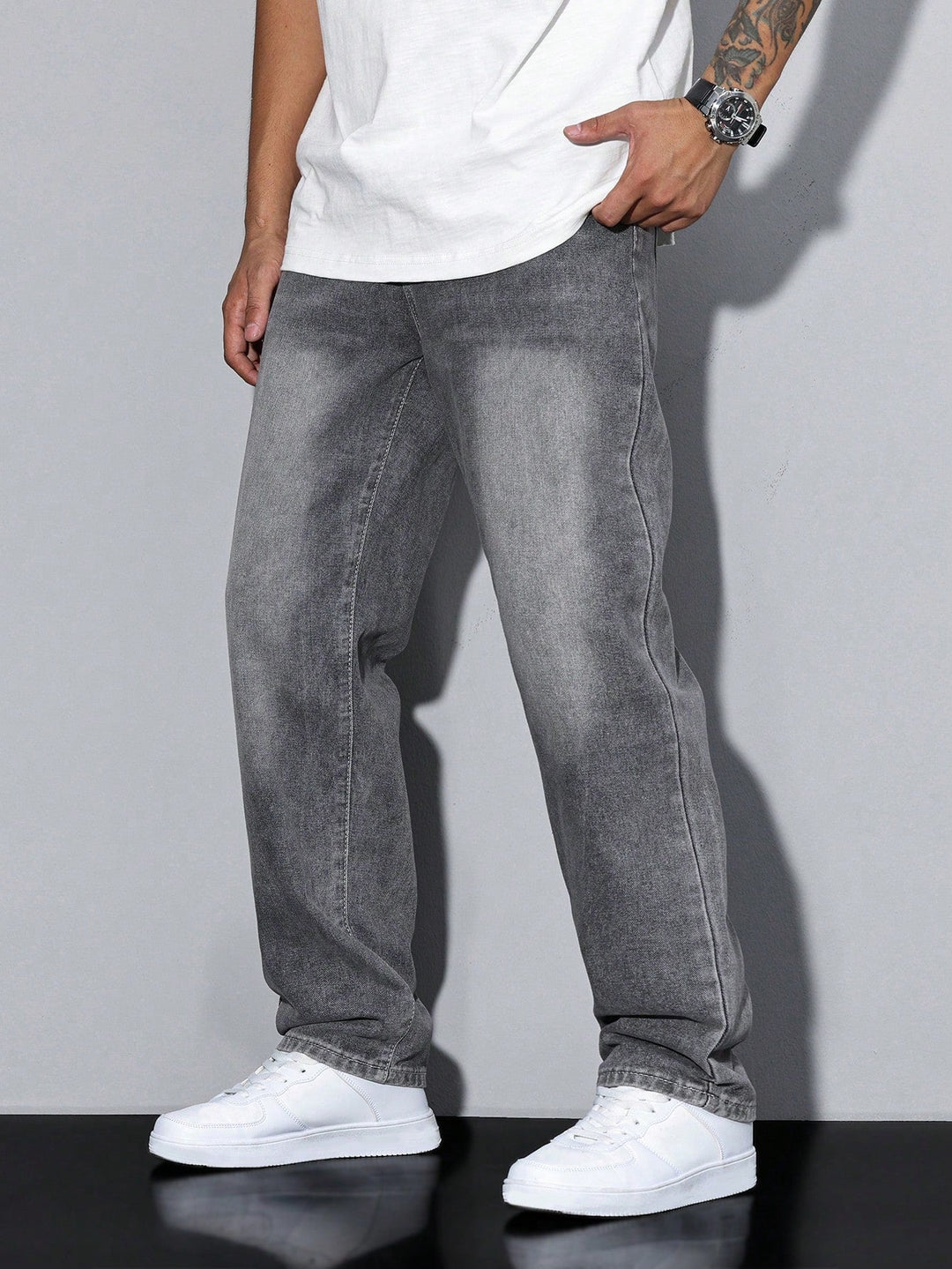 Jean gris délavé coupe large porté par un homme, vue de trois quarts, main dans la poche, avec baskets blanches. 1