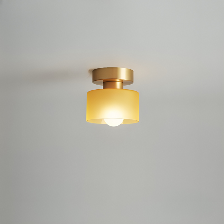 Spot à base dorée et abat-jour jaune ambré dépoli, allumé, fixé au plafond gris clair. 9