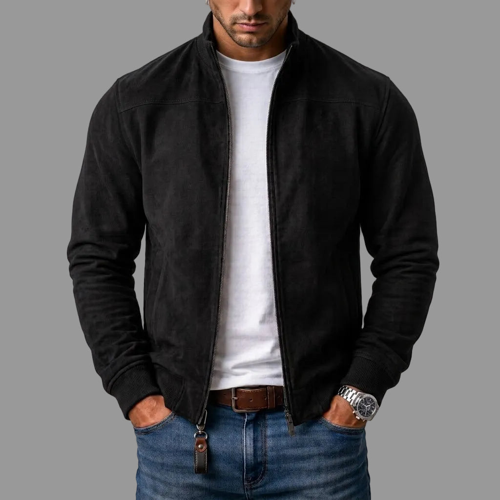 Homme portant le blouson en daim noir zippé ouvert sur un t-shirt blanc, avec jean et ceinture marron, mains dans les poches. 1