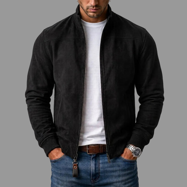 Homme portant le blouson en daim noir zippé ouvert sur un t-shirt blanc, avec jean et ceinture marron, mains dans les poches. 1