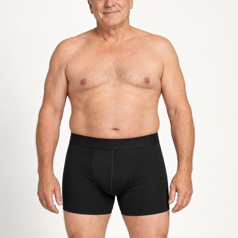 Homme mûr souriant, torse nu, portant un boxer noir à jambe mi-longue, vu de face sur fond blanc. 2