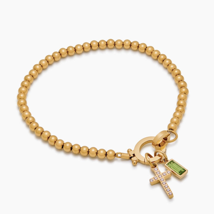 Bracelet de perles dorées vu en perspective, avec croix sertie de strass et pierre verte rectangulaire suspendues au fermoir rond. 8