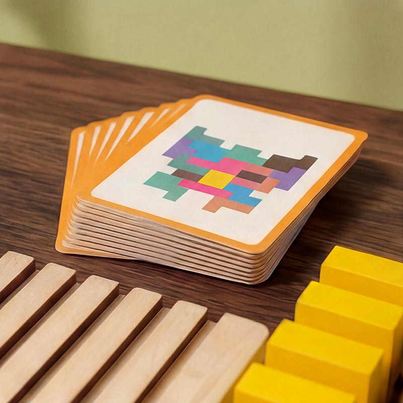 Pile de cartes modèles à bordure orange éventaillées sur une table en bois, avec des pièces jaunes et le plateau au premier plan. 9