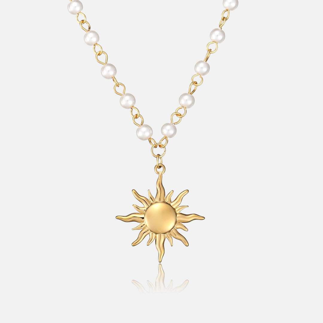 Pendentif soleil doré aux rayons ondulés suspendu à une chaîne dorée ornée de perles blanches, vue de face sur fond clair. 1