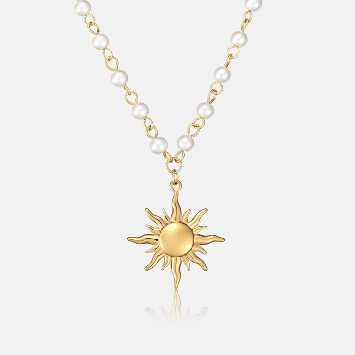Pendentif soleil doré aux rayons ondulés suspendu à une chaîne dorée ornée de perles blanches, vue de face sur fond clair. 1