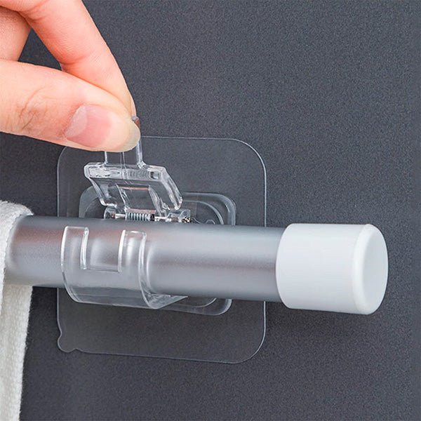 Gros plan d'une main qui pince la languette d'un support adhésif transparent à ressort pour y fixer une barre sur un mur gris. 2