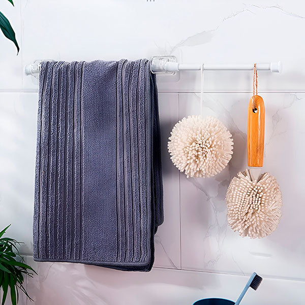 Salle de bain en marbre blanc où une barre fixée par un support transparent porte une serviette grise et deux éponges en boule. 9