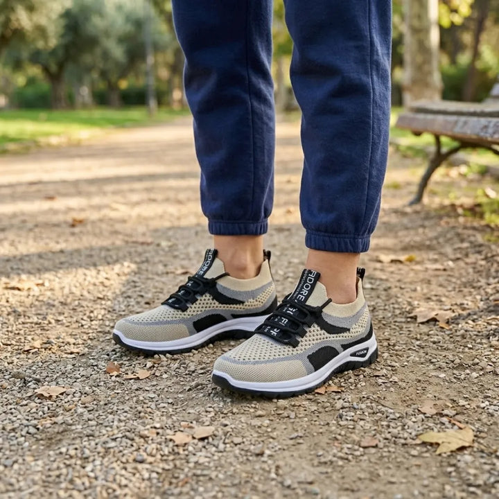 Pieds portant des baskets beige, gris et noir avec un pantalon de jogging bleu marine, sur un chemin de parc près d'un banc. 38