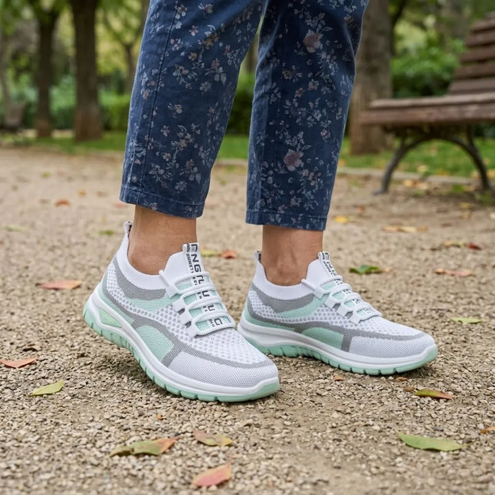 Paire de baskets blanches et vert menthe portée avec un pantalon bleu à fleurs, devant un banc de parc. 11