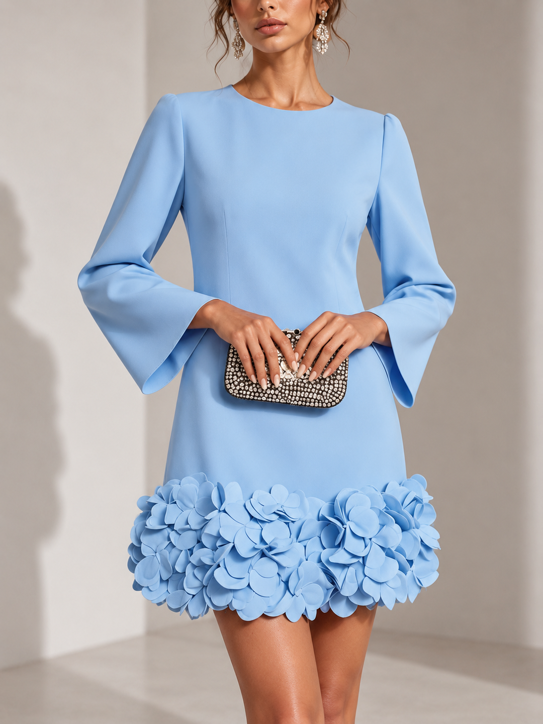 Robe bleu ciel portée de face, mains jointes sur une pochette strassée, bas orné de fleurs en relief. 5