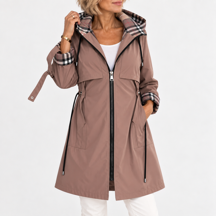 Manteau mauve taupe zippé porté par une femme, capuche relevée, doublure à carreaux visible, une main dans la poche. 1