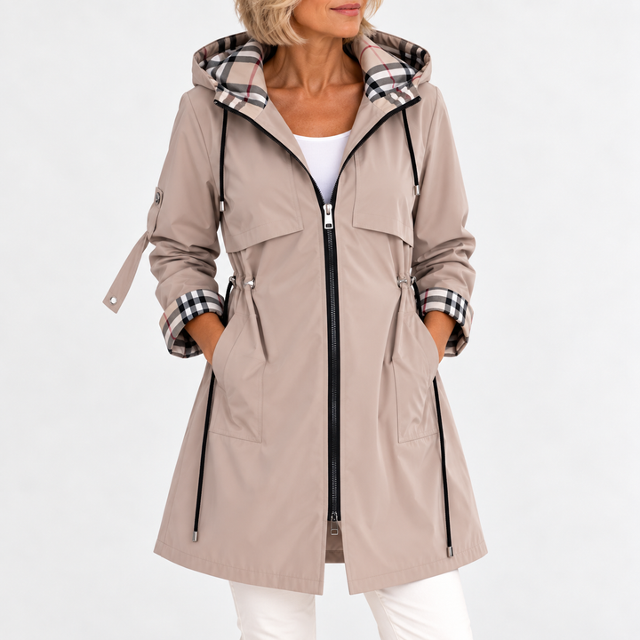 Manteau beige zippé vu de face sur une femme, mains dans les poches, taille resserrée par cordons et doublure à carreaux. 2