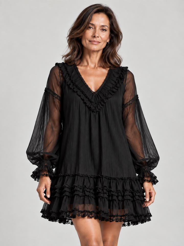 Femme portant la robe noire en plan rapproché de face, avec volants autour du col en V et manches transparentes. 1