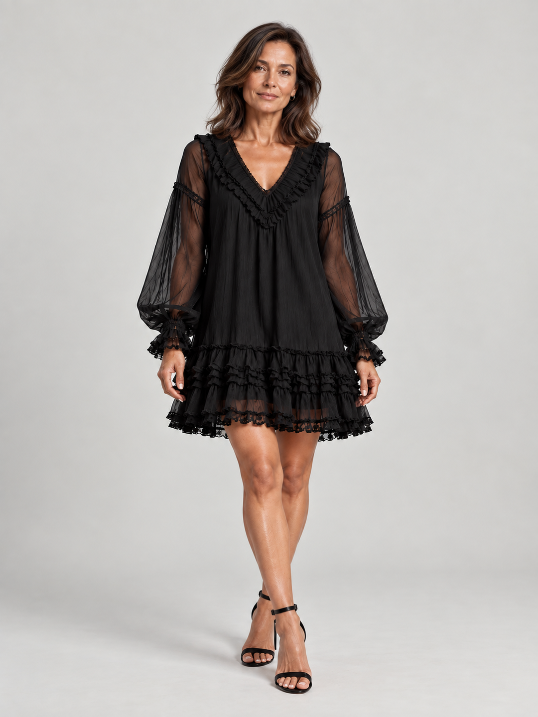 Robe noire portée en pied, vue de face, avec sandales à talons, jupe à volants superposés et manches transparentes. 2