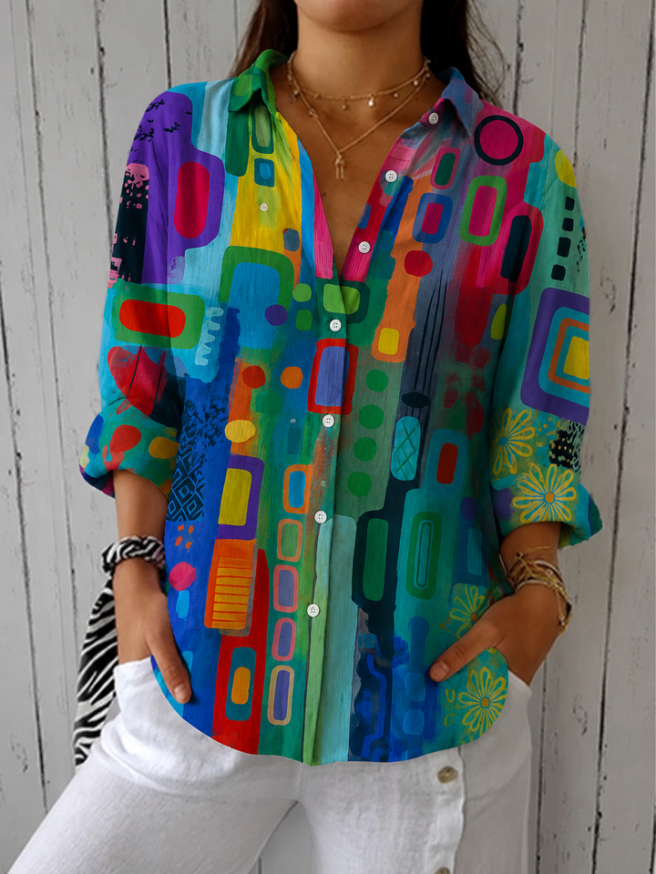 Blouse boutonnée à col chemise et motif abstrait multicolore vert, bleu, rouge et jaune, portée avec un pantalon blanc. 2