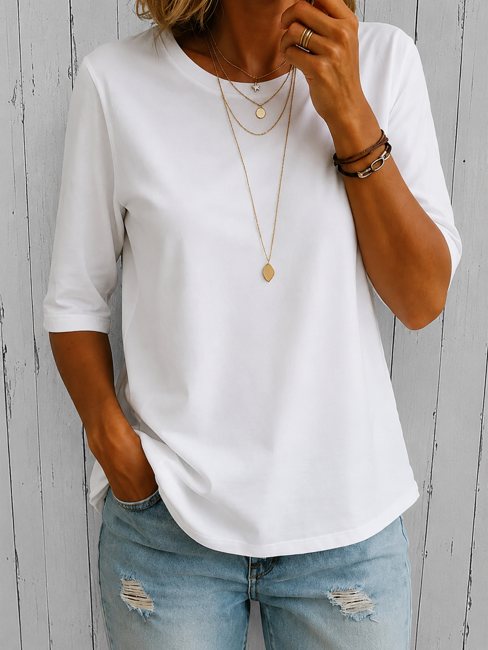 T-shirt blanc à col rond et demi-manches porté par un mannequin, mains dans la poche du jean, devant un mur en lattes. 2