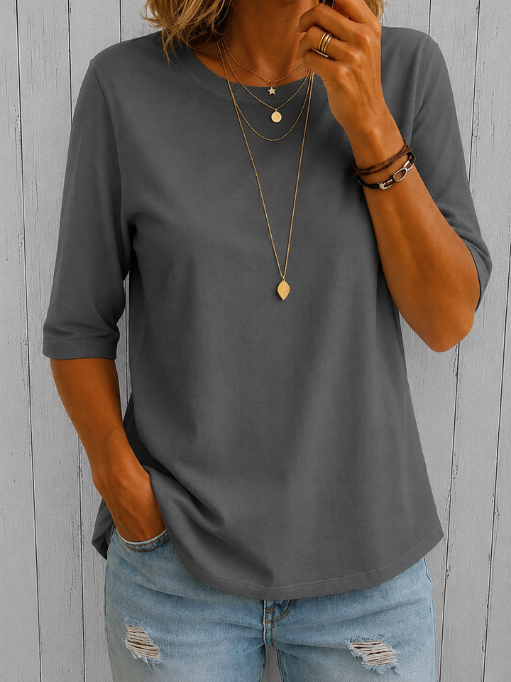 T-shirt gris foncé à demi-manches, col rond, porté avec un jean troué et des bracelets, devant un mur de lattes grises. 9